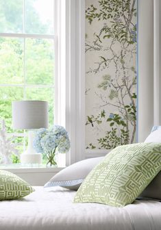 a white bed with green and blue pillows in front of a wallpapered window