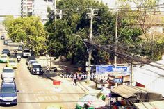 cars are driving down the street in front of buildings and power lines, with people walking on the sidewalk