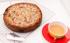 a cake sitting on top of a cooling rack next to a cup of tea and spoon