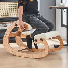 a man sitting on top of a wooden rocking chair in front of a computer desk