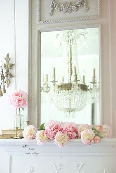 pink flowers are sitting on the mantle in front of a mirror and chandelier