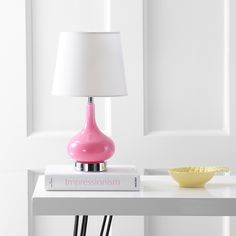 a pink lamp sitting on top of a white table next to a bowl and book