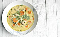 a bowl of soup with carrots, celery and other vegetables on a white wooden table