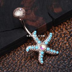 a blue and white starfish belly button ring on a black cloth with an ocean themed background