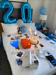 a birthday cake on a bed with blue balloons and other items around it that spell out the number 20