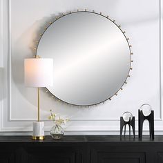 a large round mirror sitting on top of a dresser next to a lamp and vase