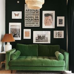 a green couch in front of a black wall with pictures on it and a lamp