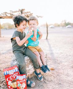 two young boys sitting on top of a rock eating ice cream and crackers in front of them