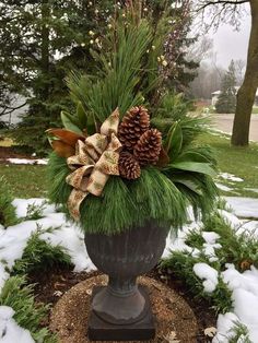 a potted plant with pine cones and greenery in the middle of snow covered ground