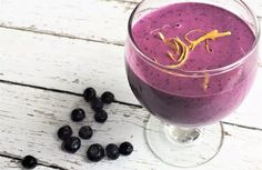 a purple smoothie in a glass next to some blackberries on a white wooden table