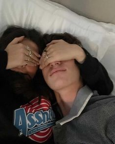 a man and woman laying in bed with their hands on each other's forehead