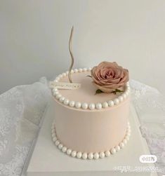 a pink cake decorated with pearls and a single rose on top is sitting on a white tablecloth