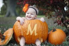 a baby sitting in a pumpkin with the letter m on it