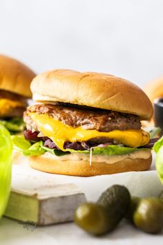 two hamburgers with cheese and lettuce on a cutting board next to olives