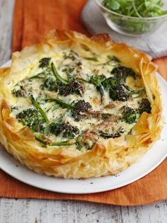 a quiche with broccoli and cheese is on a plate next to a bowl