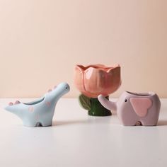 three ceramic elephants are sitting next to each other on a table with a pink wall behind them