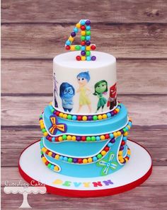 a three tiered cake decorated with cartoon characters and candy beads on a wooden table