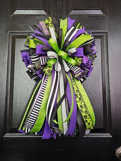 a purple, green and black wreath is hanging on the front door with ribbon around it