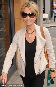 an older woman walking down the street with her hand in her pocket and wearing sunglasses