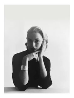 a black and white photo of a woman with her hand on her chin, sitting at a table