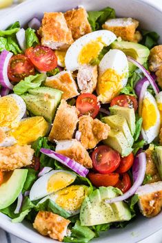 a salad with eggs, avocado, tomatoes and croutons in it