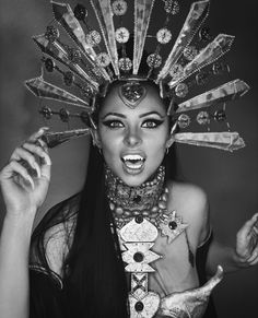 a woman with long hair wearing an elaborate headdress and holding her hands up to her face