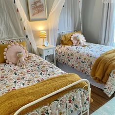 two beds in a room with white curtains and yellow comforters on top of them