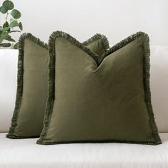 two green pillows sitting on top of a white couch next to a potted plant