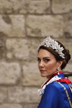 the queen is wearing a tiara and standing in front of a brick wall