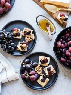 grapes and crackers are on black plates next to cheese, honey, and olives