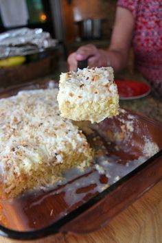 a person holding a piece of cake with coconut toppings on it, in front of a pan