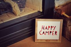 a sign that says happy camper next to a fireplace