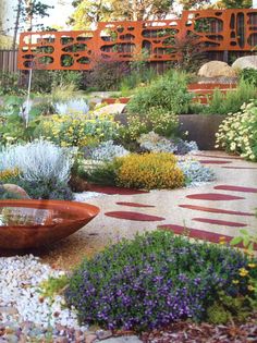 a garden with lots of different plants and flowers in it, including an orange building