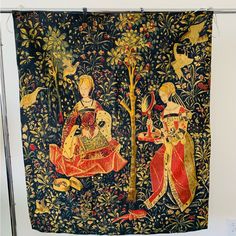 an old tapestry hanging on a wall with two women sitting in front of a tree