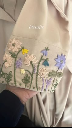 someone is holding a purse with flowers embroidered on the front and side, while wearing a white jacket