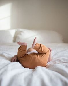 a baby laying on top of a bed in a room with white sheets and pillows