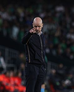 a bald man points at something while standing on the sidelines in front of an audience