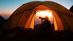 a person sitting inside of a tent with the sun setting in the distance behind them