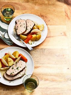 two white plates topped with meat and veggies on top of a wooden table