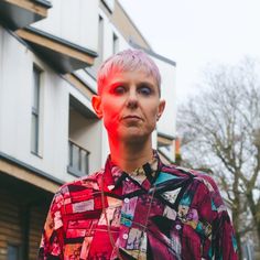 a woman with pink hair standing in front of a building and looking at the camera