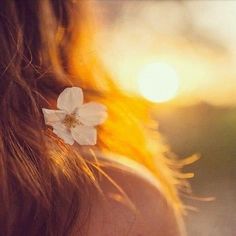 the back of a woman's head with a white flower in her left ear