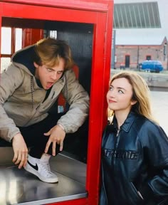 a man and woman standing in front of a red phone booth