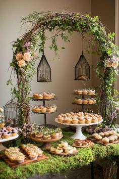 a table topped with lots of pastries covered in greenery next to a birdcage