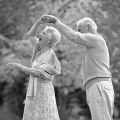 an older man and woman standing next to each other with their arms in the air