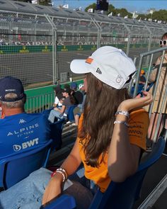 two people sitting in the stands at a race track, one is wearing a hat