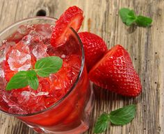 a glass filled with ice and strawberries sitting on top of a wooden table next to green leaves