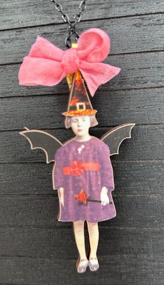 a necklace with a doll wearing a witches hat and bat wings hanging from it's side