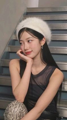 a young woman sitting on the steps with her hand under her chin and wearing a white hat