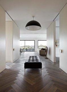 a living room with wood flooring and white walls, along with a black ottoman