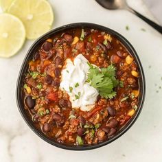 a black bowl filled with chili and sour cream on top of a white countertop